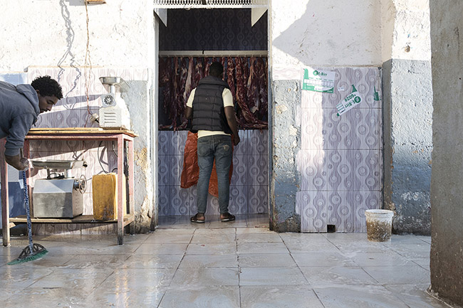 Abbas stands in front of a butcher shop at the Gidir Magala meat market in Harar, Ethiopia. 
Every morning, Abbas goes to the market dominated by butcher stalls to source fresh meat. Here, he collects up to 200 kg of camel, sheep, and goat meat and bones, which will be distributed to his proteges later in the evening.