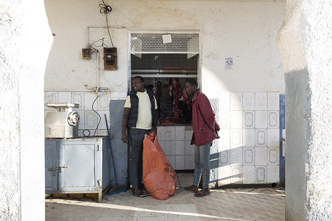 Abbas stands in front of a butcher shop, his bag filled with fresh meat. 
Every morning, Abbas goes to the market dominated by butcher stalls to source fresh meat. Here, he collects up to 200 kg of camel, sheep, and goat meat and bones, which will be distributed to his proteges later in the evening.