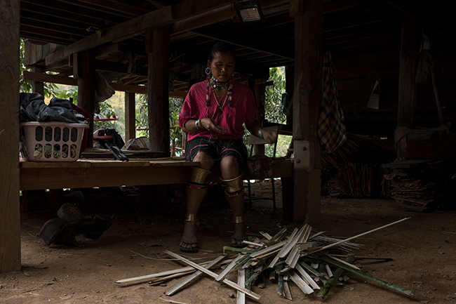 Under her wooden house built on stilts, while a Thai B-movie is played on her phone, Lei Ka, from the Kayaw ethnic group, makes thin bamboo sticks that will be used to weave teak leaves. In Huay Pu Keng, 3 families of the Kayaw ethnic group live alongside the Kayan. Unlike the Kayan, the Kayaw women do not wear rings around their necks, but rather large silver rings in the lobes of their ears. They both come from the Kayah state in Myanmar, which they fled to escape the civil war and the bloody repression in the 1980s and 1990s. These two ethnic groups would not live together in their home country. Here in Thailand - because of their unusual appearance - the Kayaw have been settled in Huai Pu Kaeng alongside the Kayan.