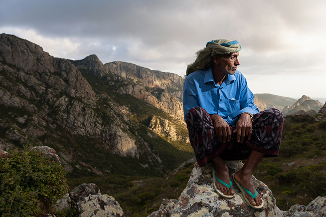 Issa, a camel man, standing at the Daadha pass in front of the granite Haggier mountains. Socotra - Yemen - 2020