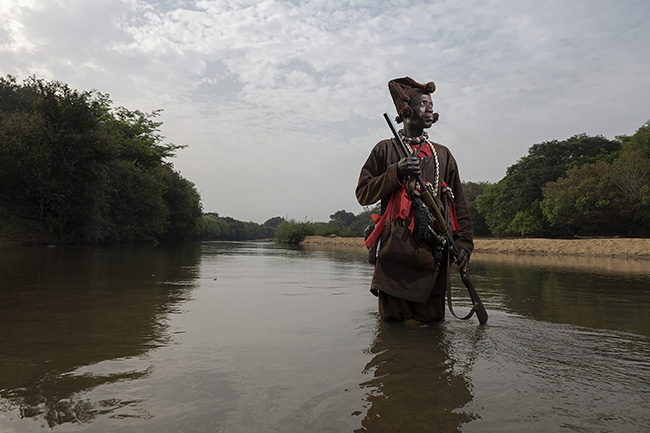 Traditional Donzo hunter walking in the Niger River in Guinea. Even though they have no legal status, due to their extensive knowledge of the bush, Donzo hunters assist the Guinean government in protecting the environment and combating poaching.